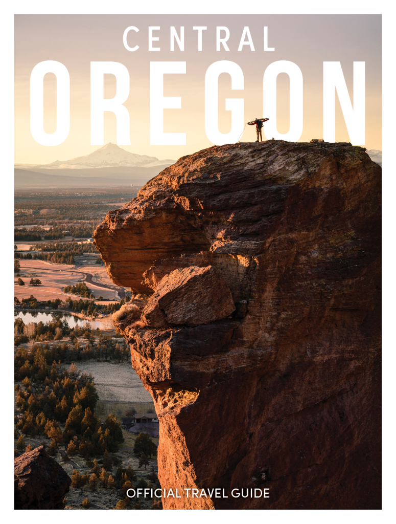 Visit Central Oregon's 2026 Travel Guide Cover of a man standing on Monkey Face at Smith Rock State Park one winter morning